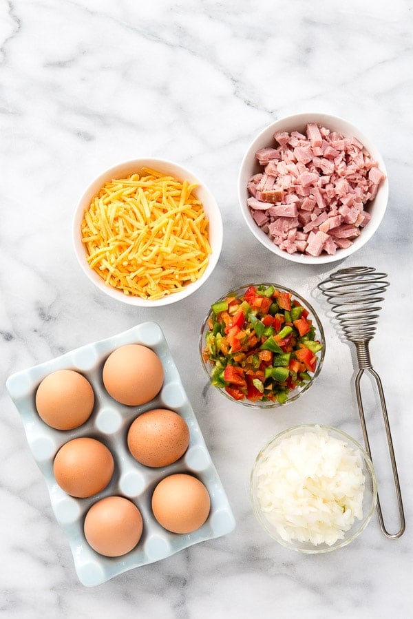 Ingredients for Muffin Tin eggs on marble slab with vintage whisk