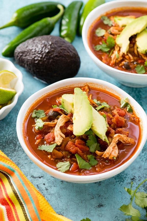Two white bowls of Instant Pot Chicken Taco Soup with avocado slices, torn cilantro leaves, lime wedges