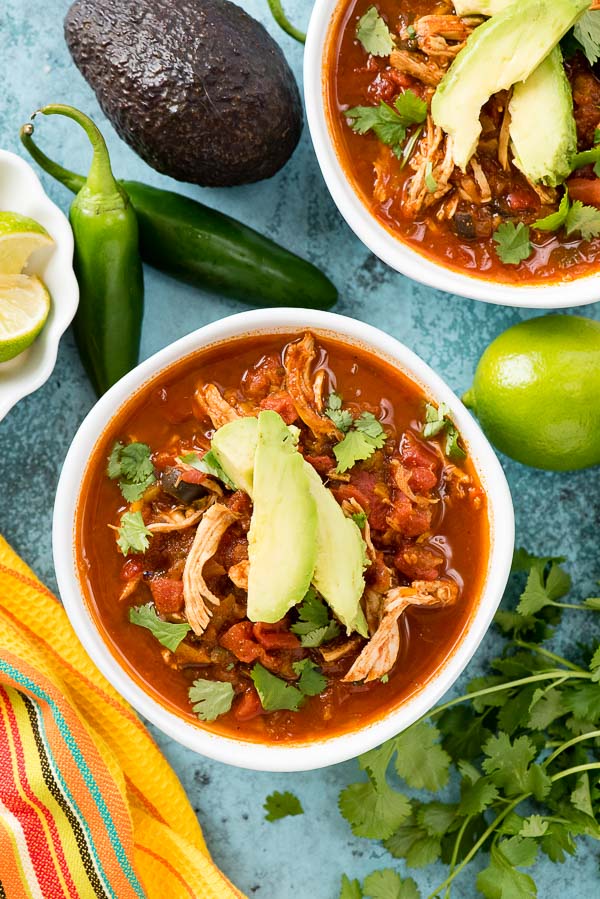 Two white bowls of Instant Pot Chicken Taco Soup with avocado slices, torn cilantro leaves, lime wedges