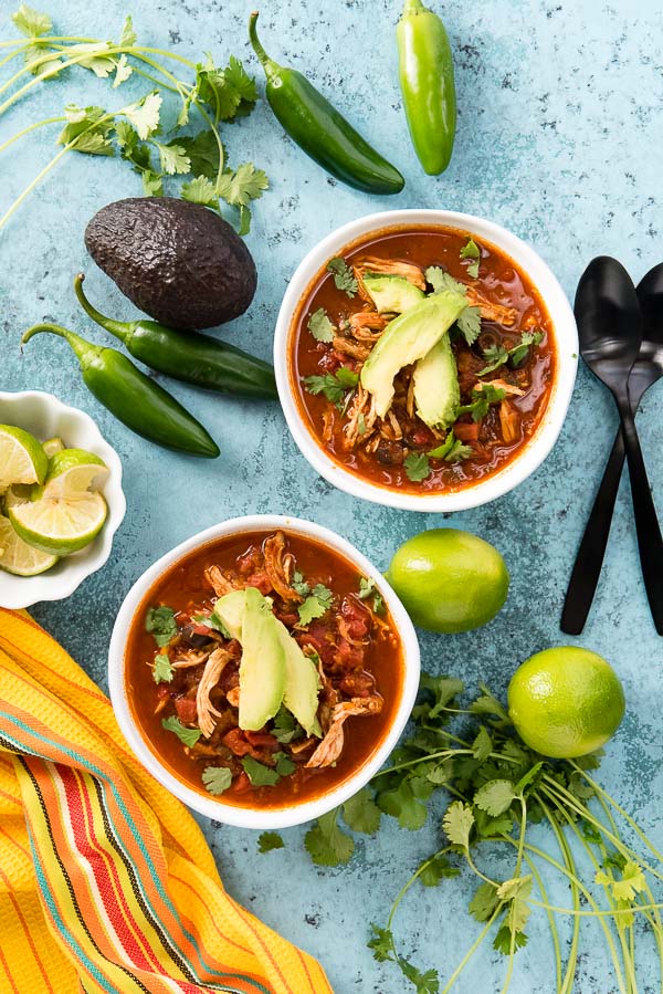 Two white bowls of Instant Pot Chicken Taco Soup with avocado slices, torn cilantro leaves, lime wedges