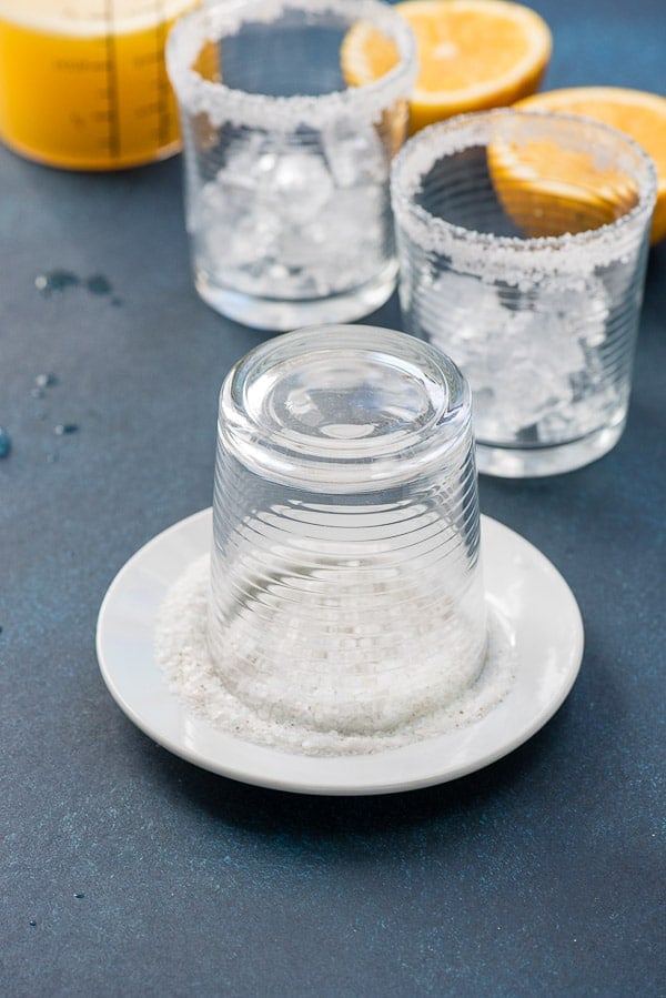 Salt rimmed Old Fashioned glasses with grapefruit juice and halved grapefruits