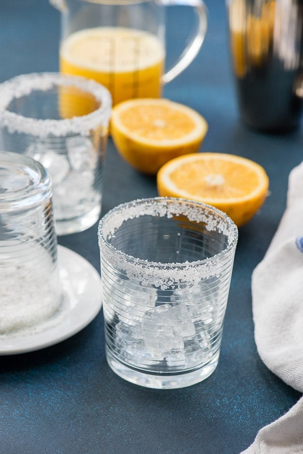 Salt rimmed Old Fashioned glasses with grapefruit juice and halved grapefruits