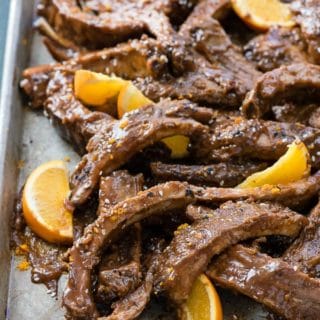 Metal baking sheet of Slow Cooker Sweet Sesame Baby Back Ribs with orange slices and sesame seeds