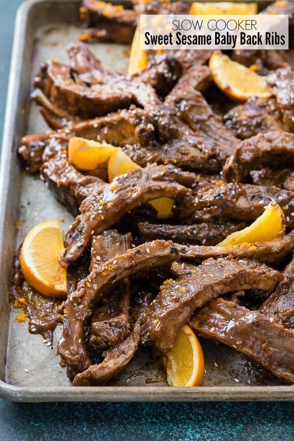 Metal baking sheet of Slow Cooker Sweet Sesame Baby Back Ribs with orange slices and sesame seeds