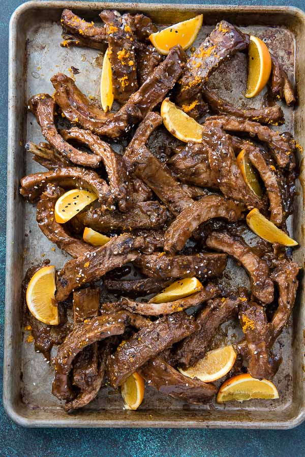 Hot batch of Slow Cooker Sweet Sesame Baby Back Ribs with orange wedges on a half baking sheet