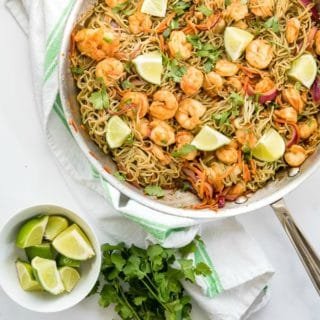 Dragon Shrimp Noodles in a large silver skillet with lime wedges and cilantro