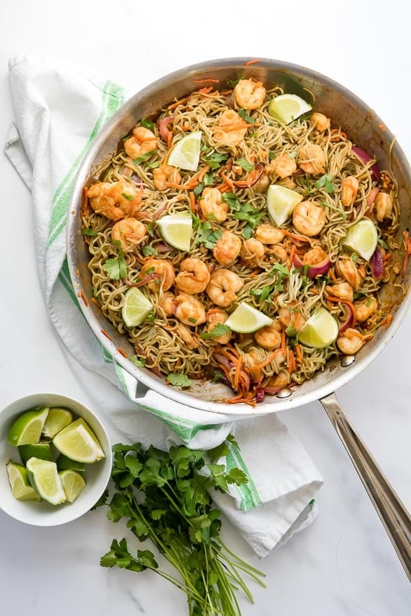 Four spicy, sweet servings of Dragon Shrimp Noodles in a large skillet with lime wedges and fresh cilantro
