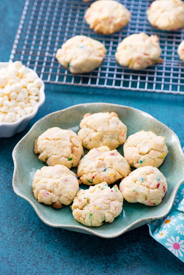 Blue ruffled edge plate with gluten-free Cake Mix Funfetti Cookies with bowl of white chocolate chips and cooling rack in background