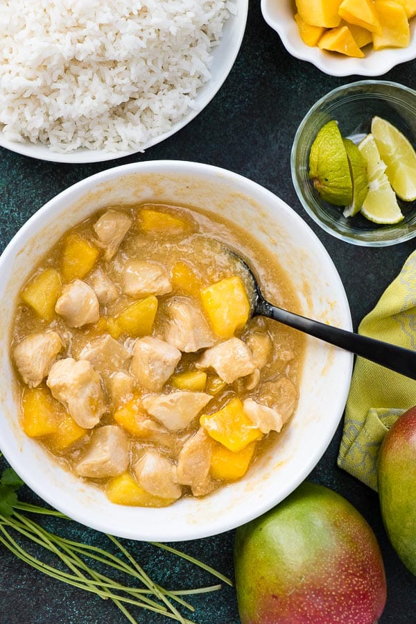 Instant Pot Mango Chicken in a large white bowl with whole mangoes, lime wedges and white rice