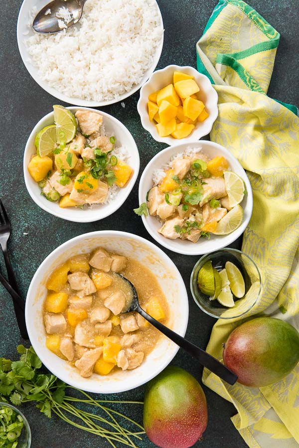 Bowls of Instant Pot Mango Chicken with white rice, cilantro, lime wedges and whole mangoes