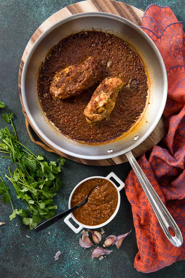 Mole-Roasted Chicken in a large skillet with cilantro. and mole sauce in a white ramekin