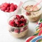 Raspberry Mocha French Vanilla Overnight Oats in glass jars piled high with fresh raspberries, dairy-free chocolate syrup and hemp hulls with red gingham spoon