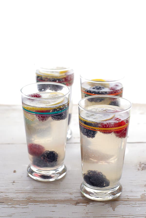 Four tall glasses of Elderflower Gin Fizz cocktails with frozen berries
