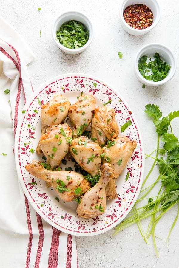 Platter of Instant Pot Ginger Soy Chicken Drumsticks with fresh cilantro and bowls of chopped cilantro, green onions and red pepper flakes
