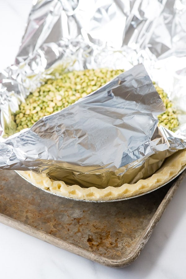 Frozen gluten-free pie crust on baking sheet with foil and beans inside for blind baking crust