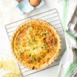 Golden Quiche Lorraine (a cheesy bacon quiche) on a cooling rack with grated cheese and eggs