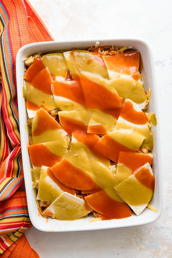 Layered easy breakfast casserole with red and green chile sauce 'christmas-style' on top before baking
