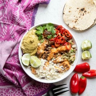 Colorful, spicy Baja Fish taco Bowl with corn tortillas, red chili peppers and lime wedges