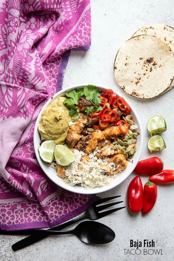 Colorful, spicy Baja Fish taco Bowl with corn tortillas, red chili peppers and lime wedges