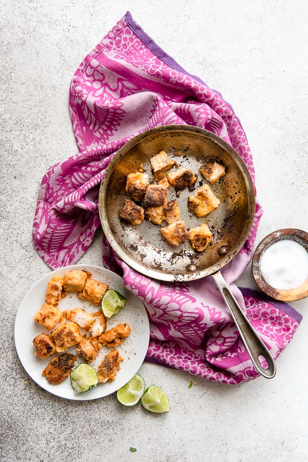 Lightly fried baja fish in saute skillet and on white plate with lime wedges