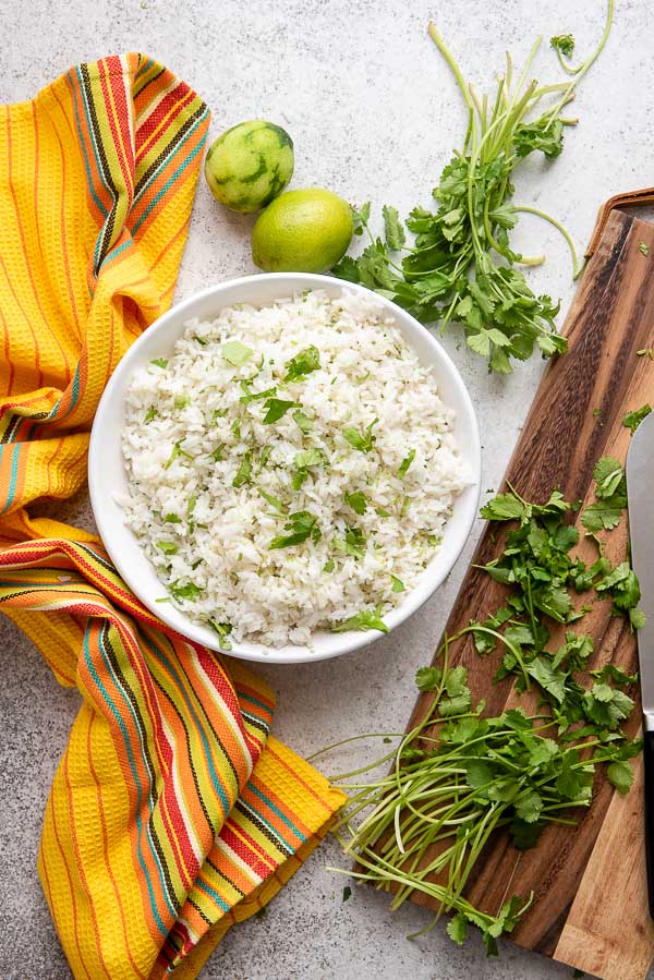 Instant Pot Cilantro Lime Rice recipe with freshly chopped cilantro on cutting board, limes and yellow Mexican kitchen towel