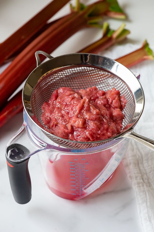 Straining cooked rhubarb to separate the pulp from the juice using a strainer over a large measuring cup