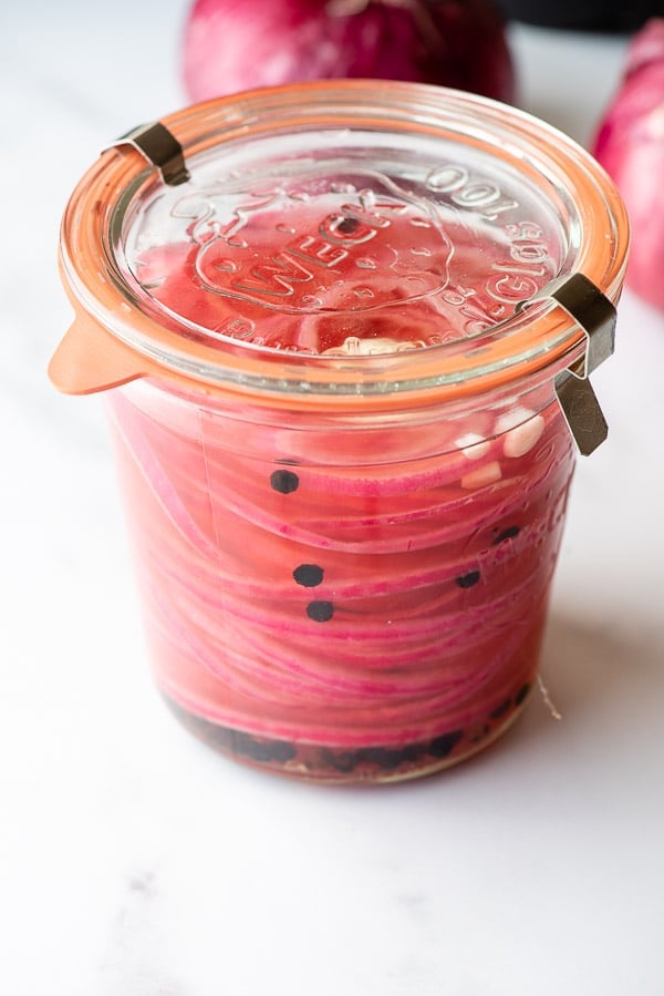 Canning jar of Quick Picked Red Onions with onions in the background