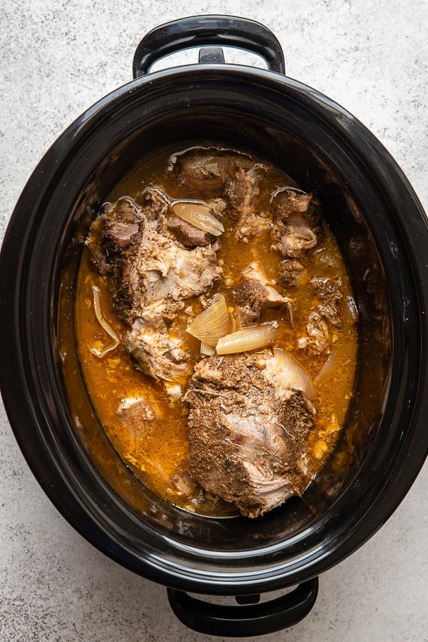 Cooked slow cooker carnitas in a black slow cooker insert with juices