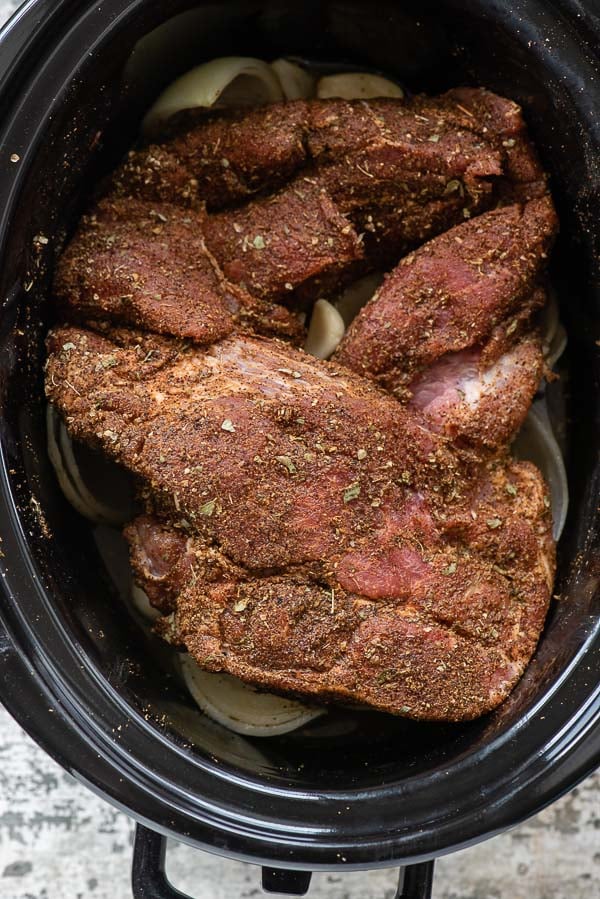 Pork shoulder with spice rub in slow cooker insert before cooking into Pineapple Citrus Slow Cooker Carnitas