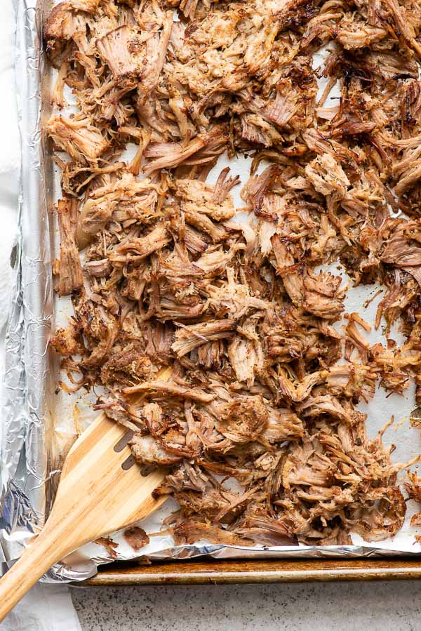 Slow cooker carnitas crisped up after broiling on a sheet pan with wooden spatula