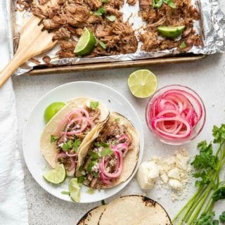 Sheet pan of Pineapple Citrus Slow Cooker Carnitas with Carnitas Tacos on a small plate, corn tortillas and quick pickled red onions