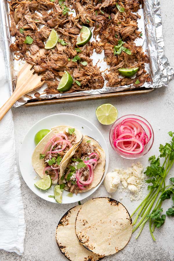 sheet pan for slow cooker carnitas with carnitas tacos, corn tortillas, pickled red onions and fresh cilantro