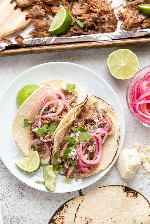 Street-style carnitas tacos with pickled red onion, lime wedges, cilantro and cotija cheese on corn tortillas
