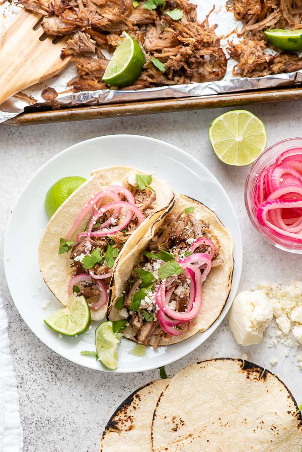 Carnitas Tacos on corn tortillas with pickled red onions, fresh cilantro leaves, lime wedges and crumbled cotija cheese