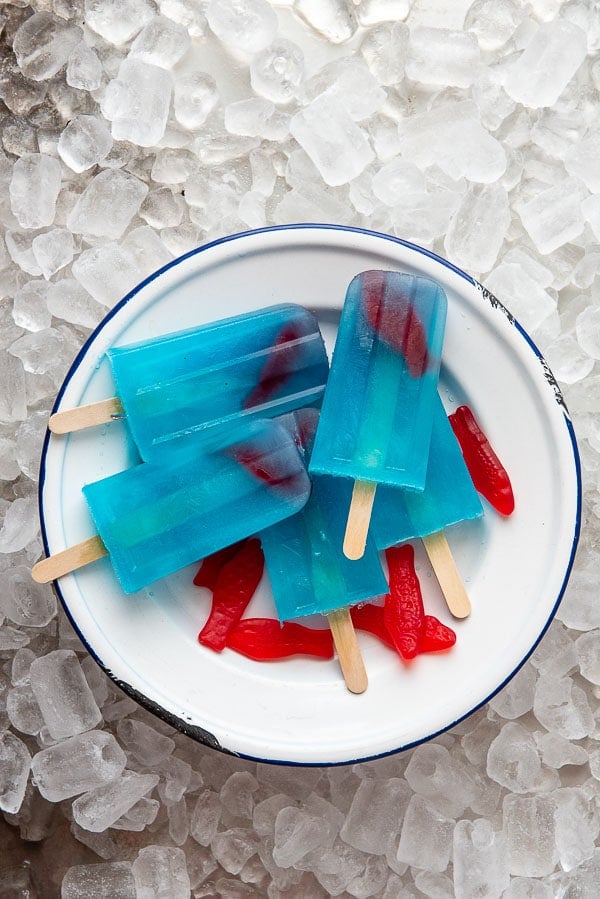 Blue Lagoon Cocktail popsciles on a white enamel plate with red Swedish fish candy