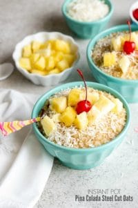 Blue bowls of Instant Pot Pina Colada Steel Cut Oats recipe with pineapple chunks, grated coconut and cherries
