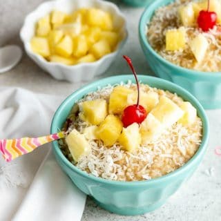 Blue bowls of Instant Pot Pina Colada Steel Cut Oats recipe with pineapple chunks, grated coconut and cherries