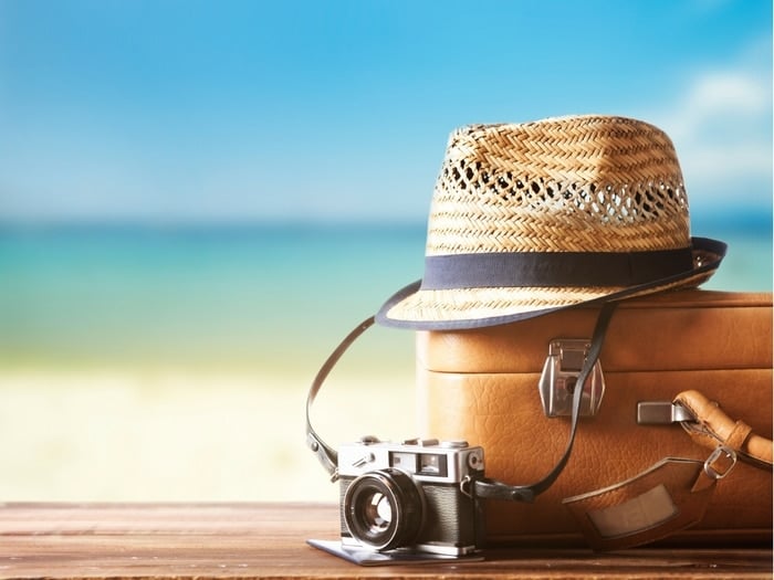 Suitcase, straw hat and camera by the beach