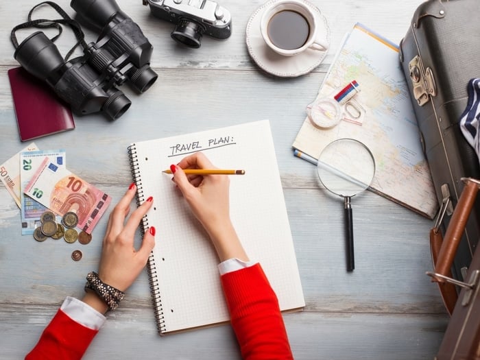 Woman writing a travel plan with travel items around on a desk