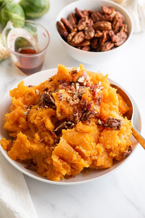 white bowl of mashed sweet potatoes with nuts and bacon on top