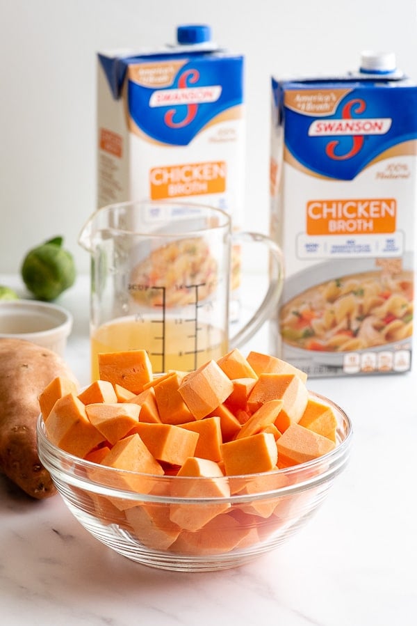 Cubed sweet potatoes in a glass bowl and chicken broth containers