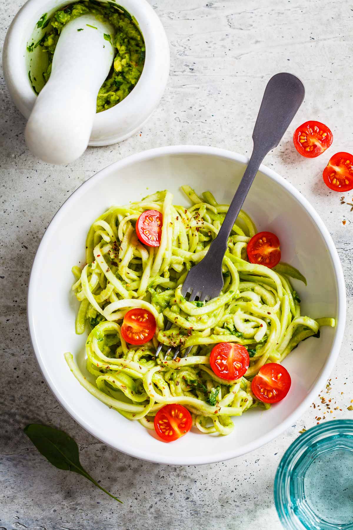 Zucchini pasta with pesto, avocado and tomatoes in white plate, top view.