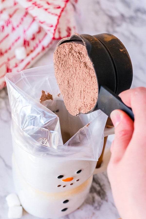 Adding hot chocolate mix to a gift bag in holiday mug