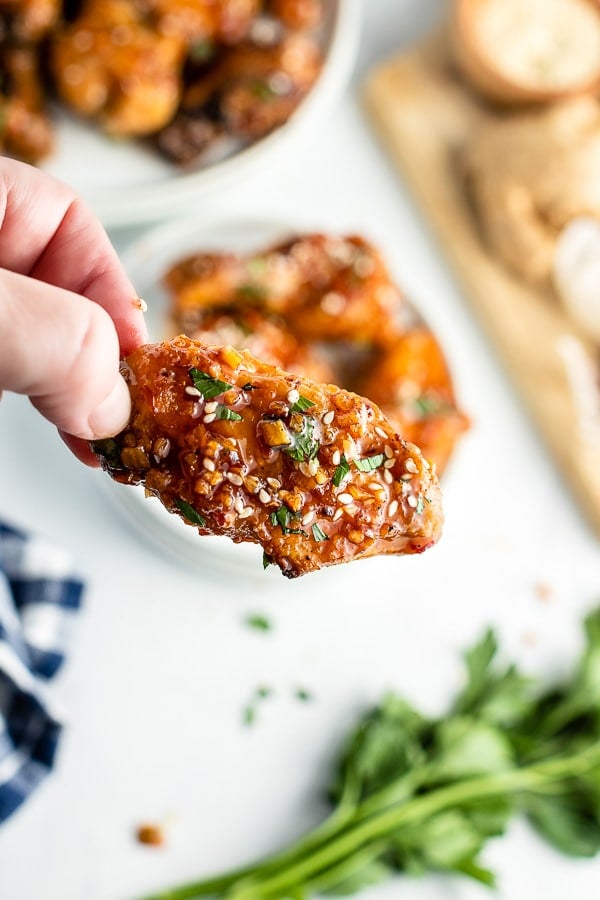 hand holding sticky grilled chicken wing with sesame seeds and diced cilantro