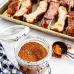 jar of Dry Rub spice mix for Ribs with baking sheet of ribs behind