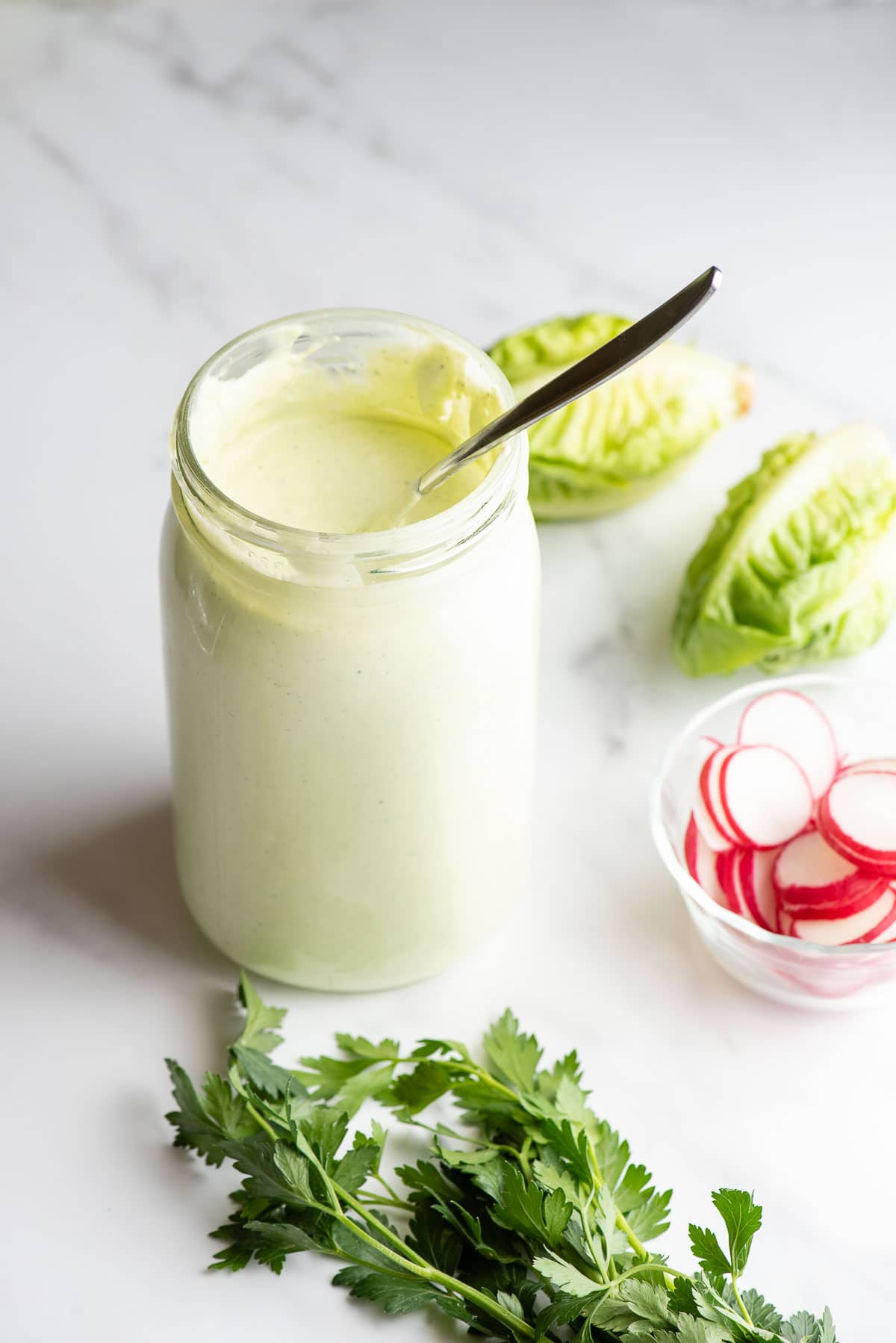 Green Goddess Dressing in a Mason jar with lettuce, parsley and sliced radishes