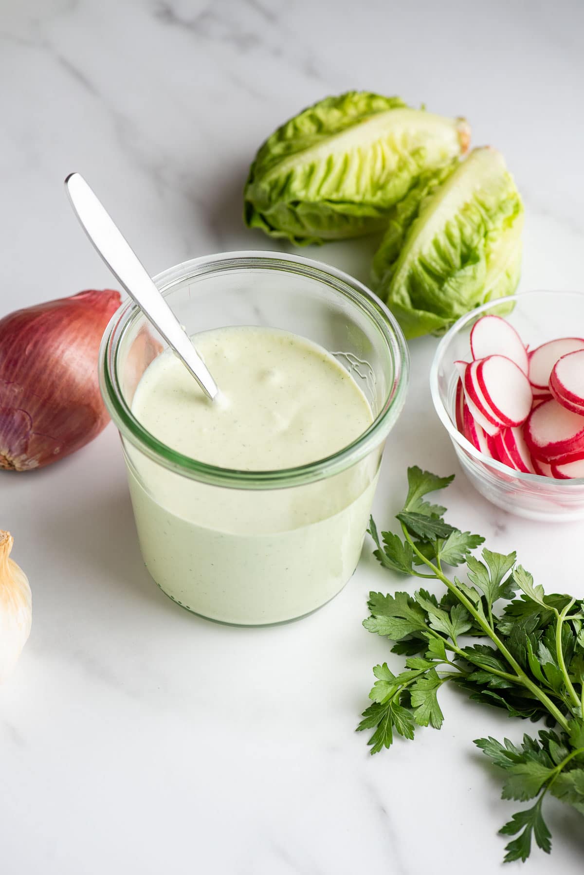 Green Goddess Dressing in a jar with spoon and fresh herbs and vegetables