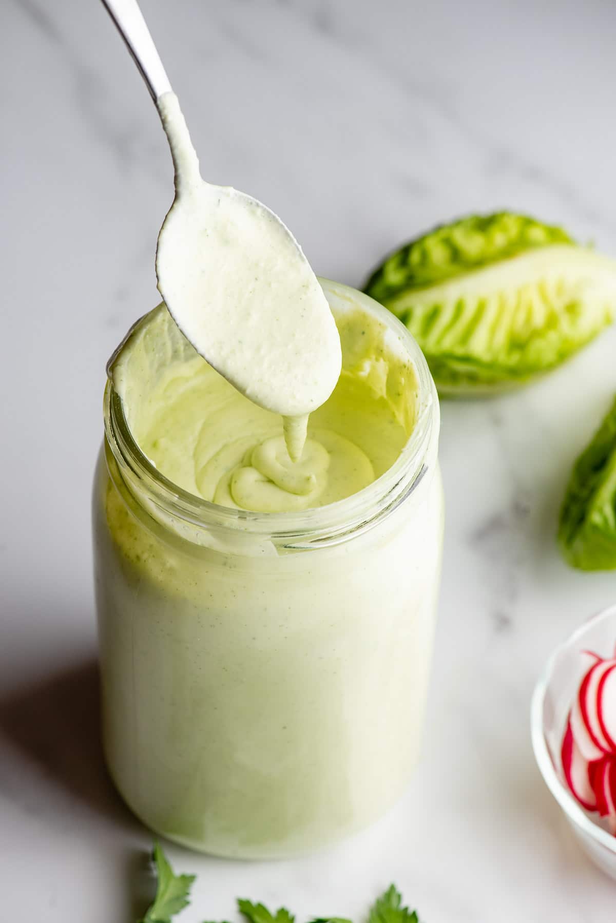 Green Goddess Dressing running off spoon into a Mason jar