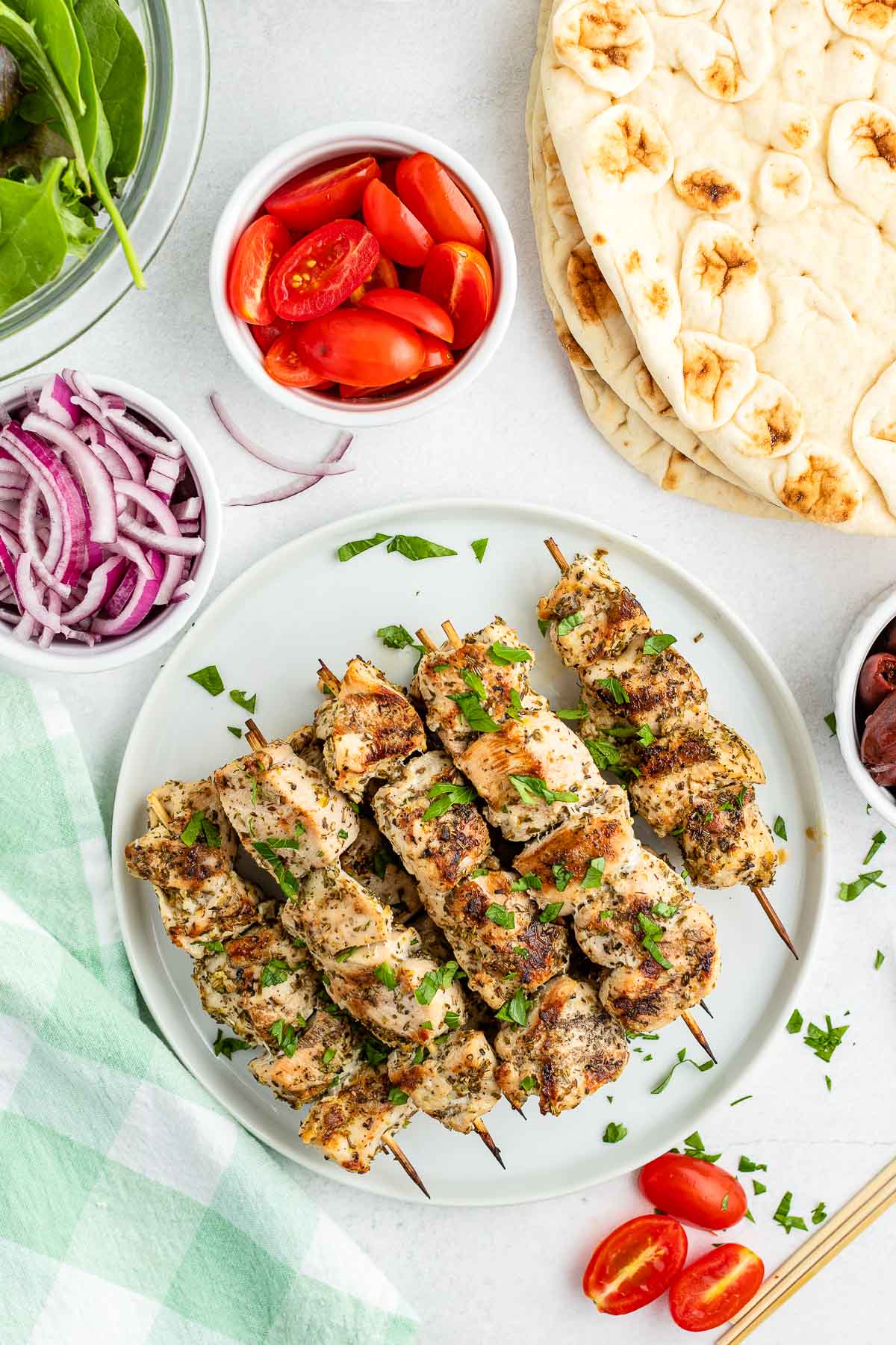 grilled chicken souvlaki skweres on a plate surrounded by containers of prepared vegetable and flatbread