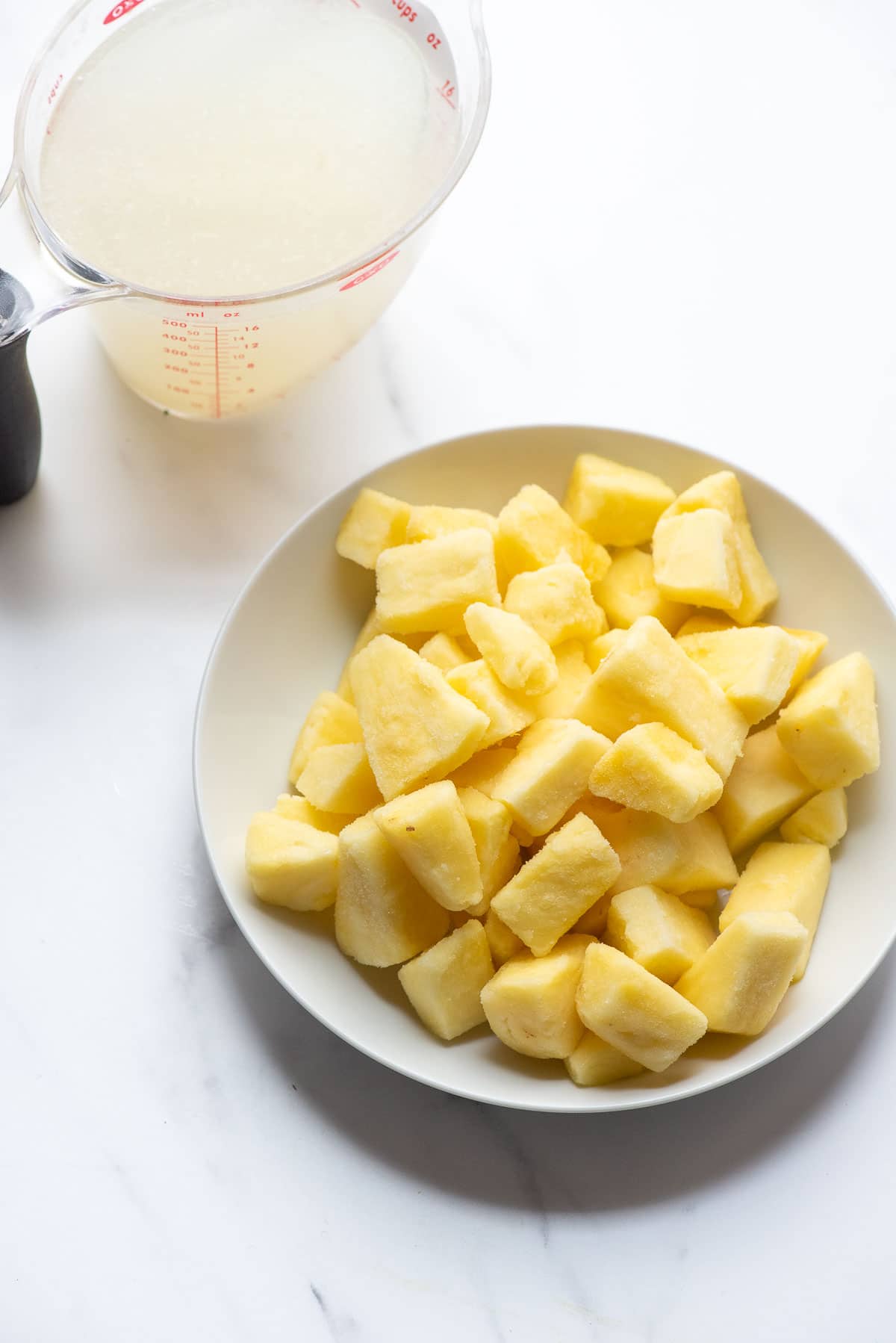 bowl of frozen pineapple and measuring cup of lemonade